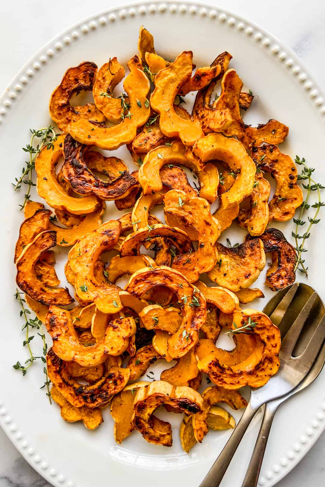 Delicata squash on a large white serving plate with a silver spoon and fork for serving.