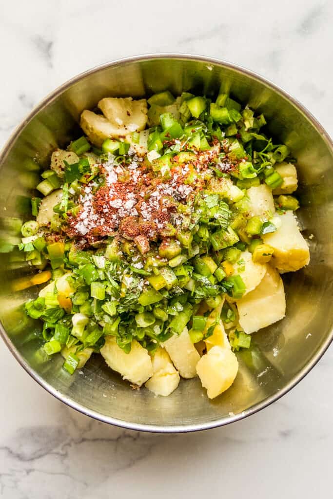 Diced potatoes, green onions, bell pepper, and spices in a large metal mixing bowl.