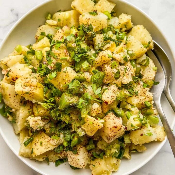 An overhead shot of a Turkish potato salad in a white serving bowl with serving serving spoons.