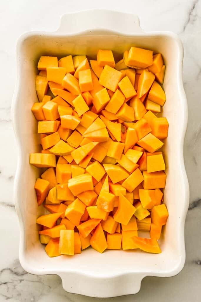 Chopped butternut squash in a white baking dish.