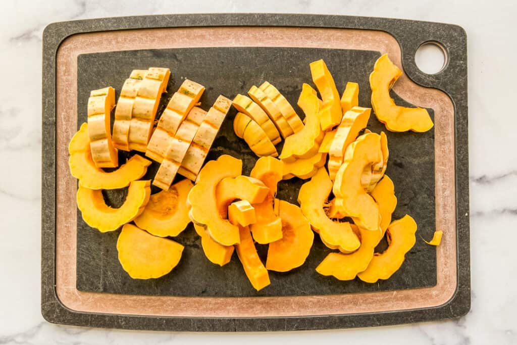 Sliced delicata squash on a black cutting board.