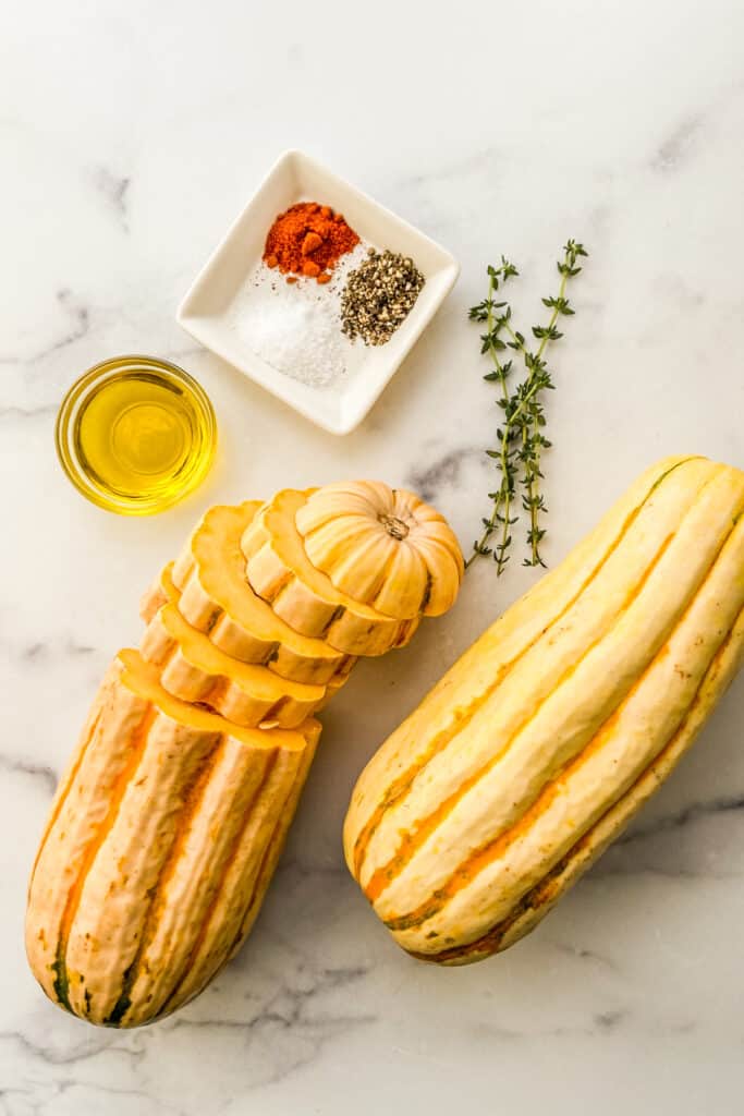 Delicata squash, olive oil, spices, and thyme on a marble background.