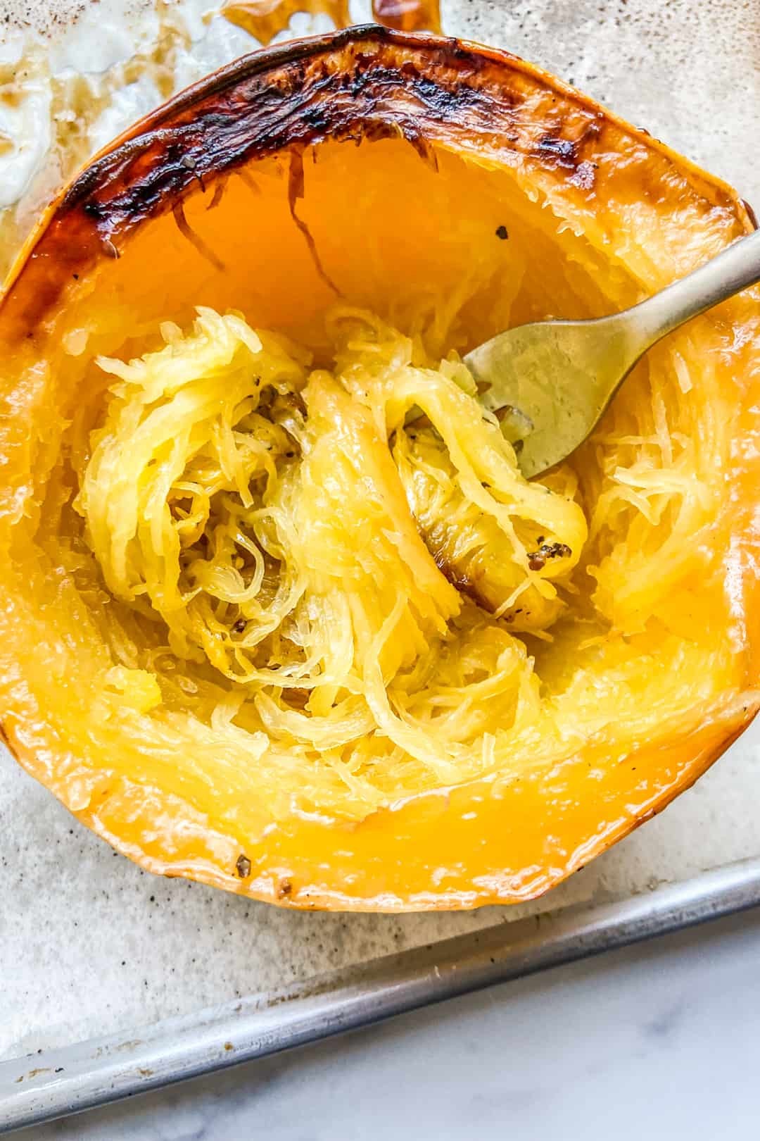 Spaghetti Squash right after roasting, with a fork removing the flesh from the skin.