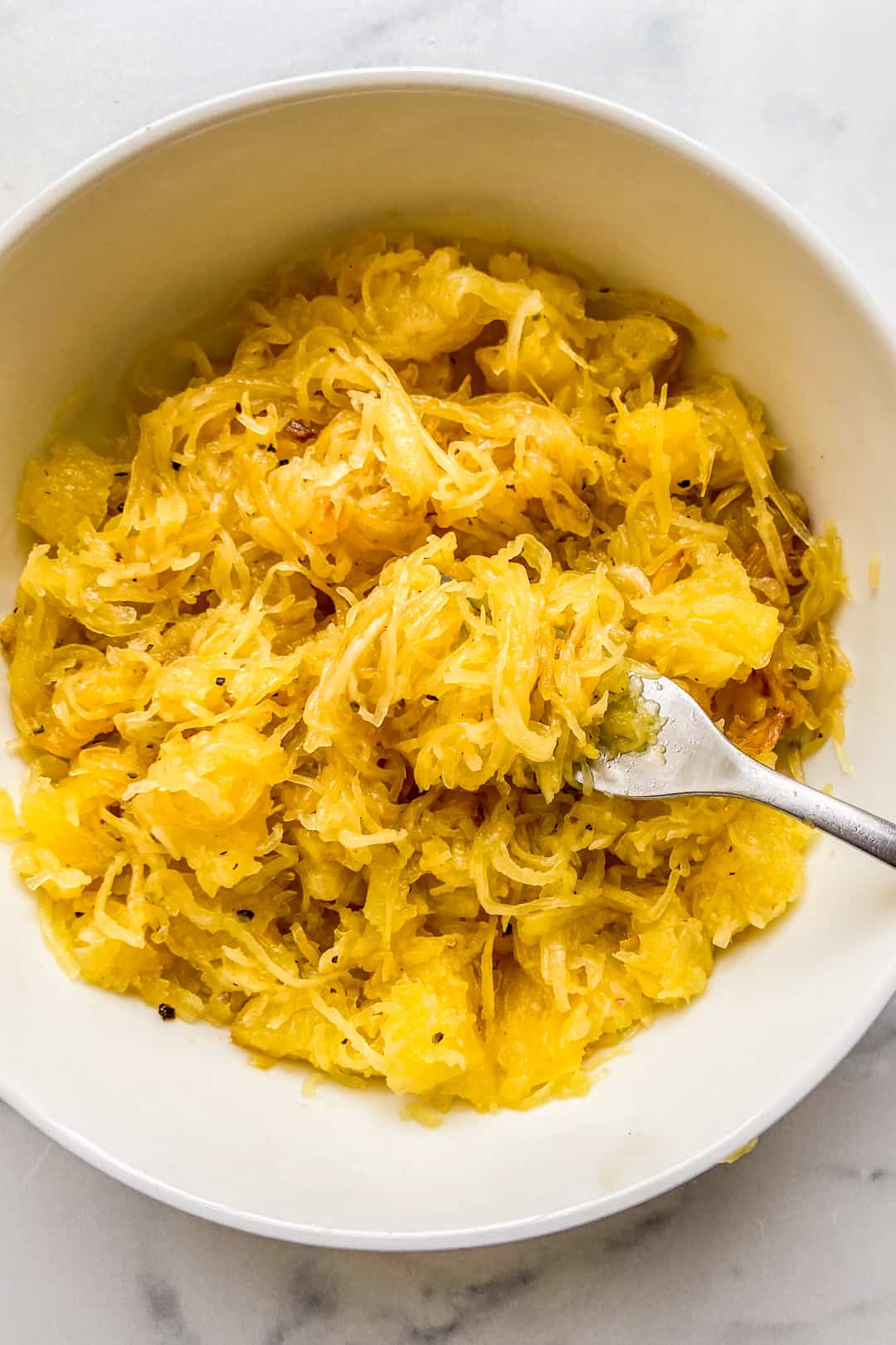 A bowl of spaghetti squash noodles with a fork twirling the noodles.