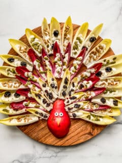 An overhead shot of a Thanksgiving turkey design made out of a pear and endives with feta dip and nuts.