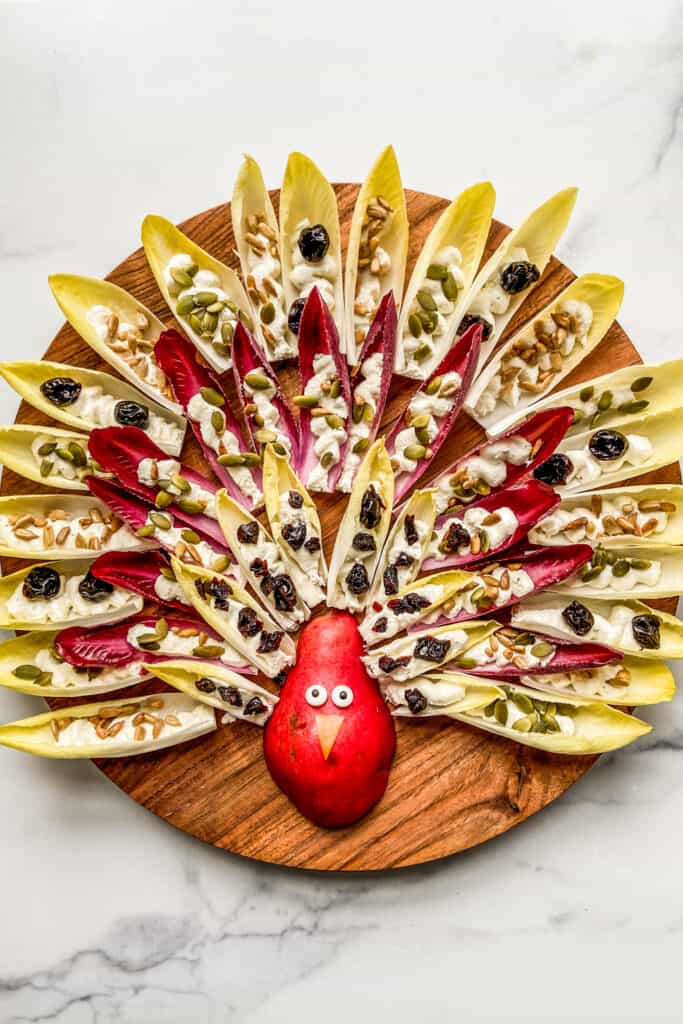 An overhead shot of a Thanksgiving turkey design made out of a pear and endives with feta dip and nuts.