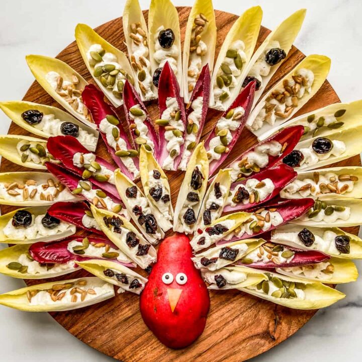 An overhead shot of a Thanksgiving turkey design made out of a pear and endives with feta dip and nuts.