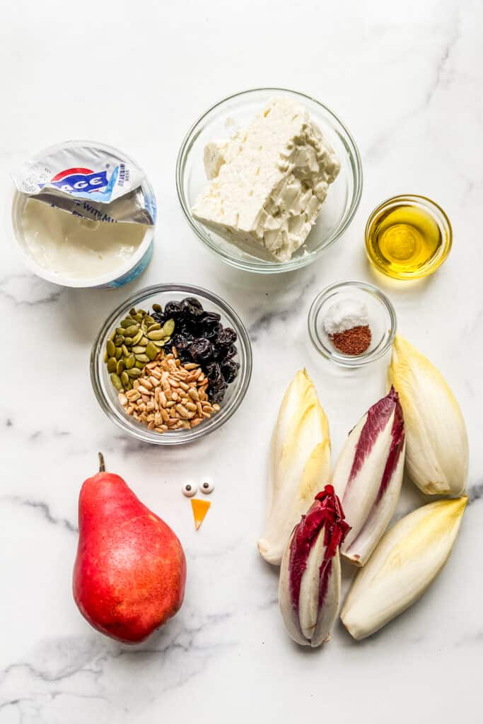 Feta cheese, yogurt, olive oil, seeds and dried fruit, endives, and a pear on a marble background.