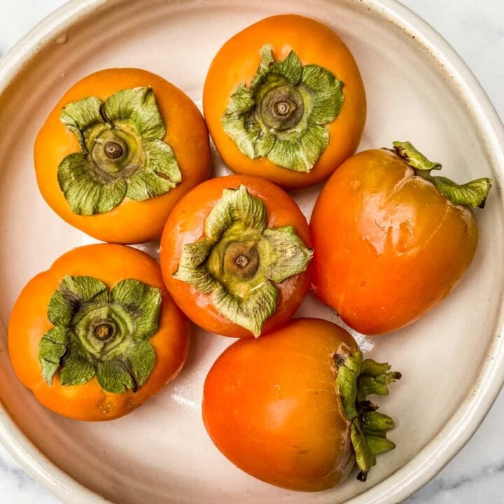 Fuyu and hachiya persimmons in a white bowl.