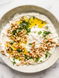 An overhead shot of a bowl of whipped feta dip topped with toasted pine nuts, olive oil, and chopped parsley.
