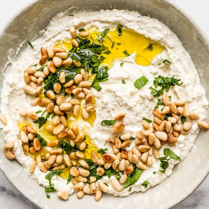 An overhead shot of a bowl of whipped feta dip topped with toasted pine nuts, olive oil, and chopped parsley.