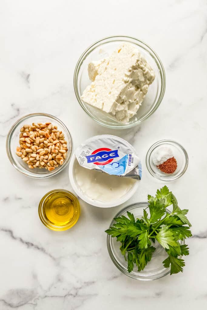 Feta, pine nuts, yogurt, sumac, salt, olive oil, and parsley on a marble background.