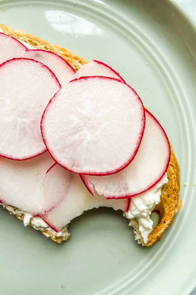 A closeup shot of a piece of toast with whipped feta and sliced radishes.