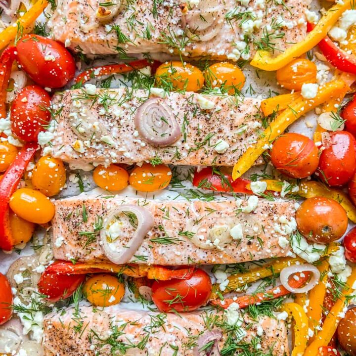 A closeup shot of four salmon fillets with roasted vegetables.