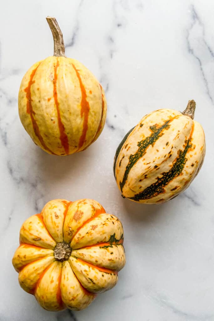 Three carnival squash on a marble backdrop.