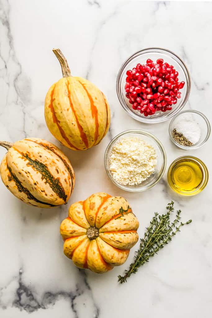 Carnival delicata squash, pomegranate, feta, salt, pepper, olive oil, and thyme on a marble background.