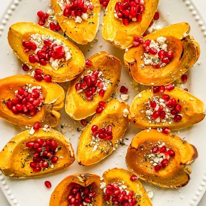 An overhead shot of a large serving platter of roasted carnival squash topped with feta and pomegranate.