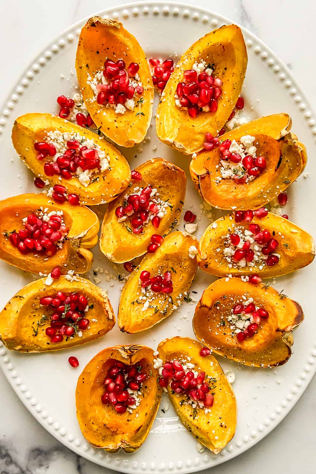 An overhead shot of a large serving platter of roasted carnival squash topped with feta and pomegranate.