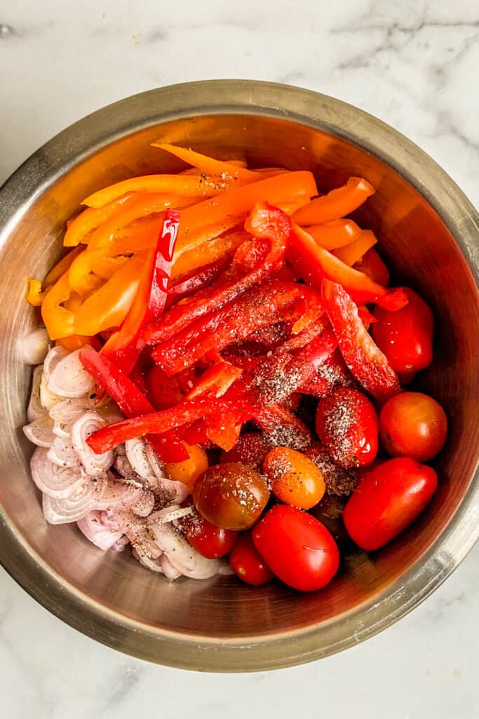 Sliced bell peppers, cherry tomatoes, and sliced shallots in a mixing bowl.