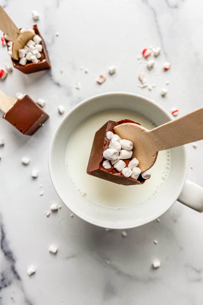 Hot chocolate on a spoon being dipped into a mug of milk.