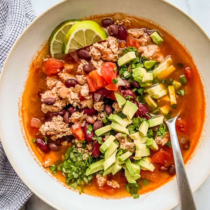 A bowl of ground chicken chili topped with avocado and cilantro.