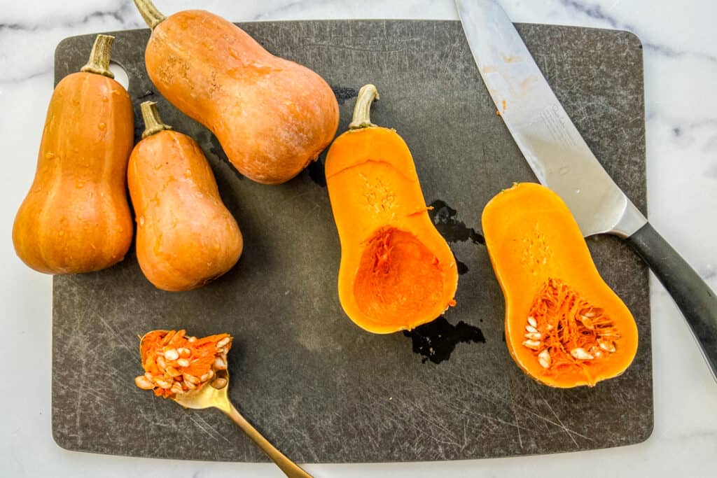 Honeynut squash being halved and the seeds scooped out on a cutting board.