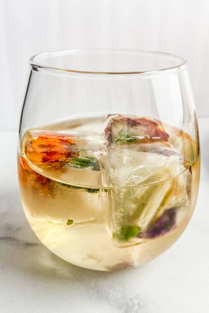 A wine glass with white wine and floral ice cubes.