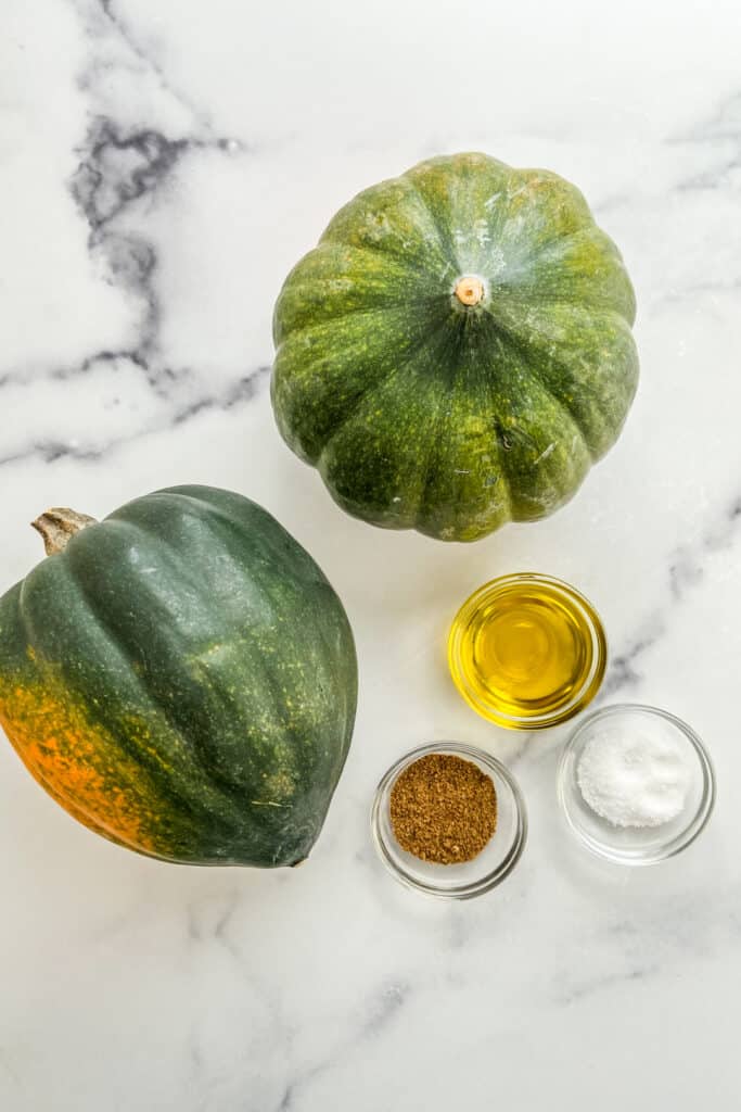 Two acorn squash, olive oil, Chinese five spice, and salt on a marble background.