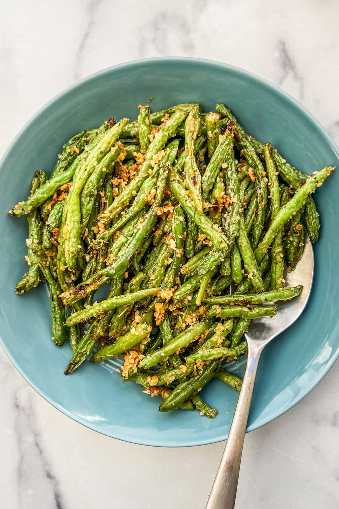 Parmesan panko green beans in a blue serving bowl with a silver serving spoon.