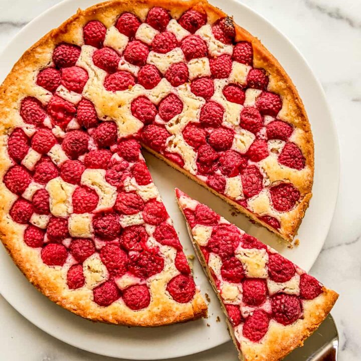 A raspberry cake on a white plate with a piece cut out on a cake scooper.