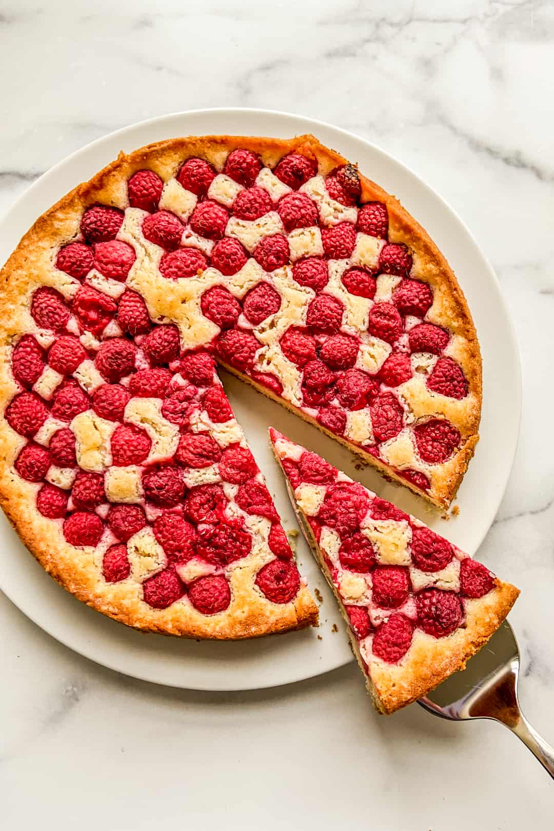 A raspberry cake on a white plate with a piece cut out on a cake scooper.