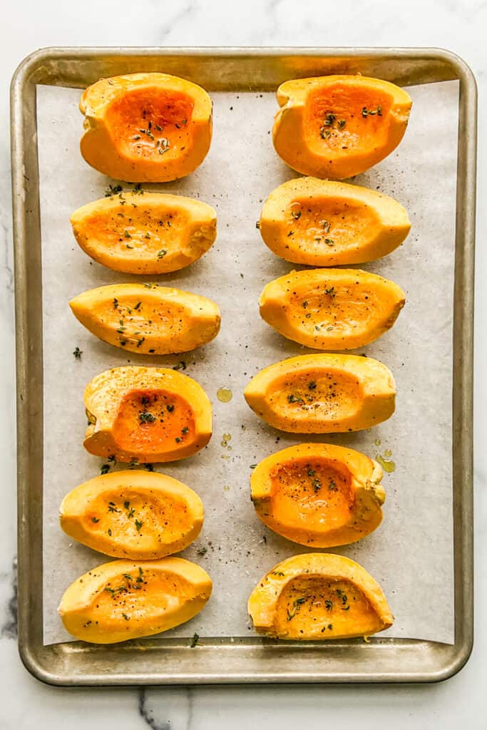 Quartered carnival squash on a baking sheet, brushed with olive oil and topped with thyme.