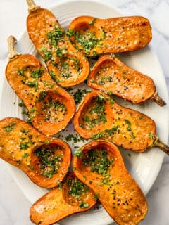 A platter of roasted honeynut squash, topped with sesame seeds and chopped cilantro.