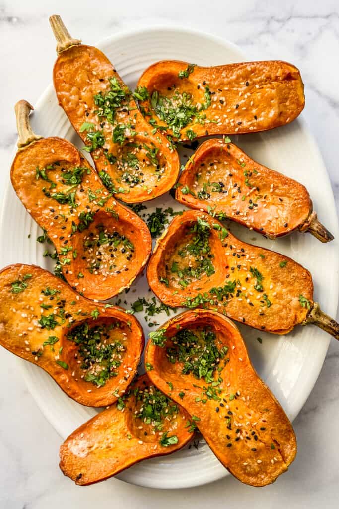 A platter of roasted honeynut squash, topped with sesame seeds and chopped cilantro.