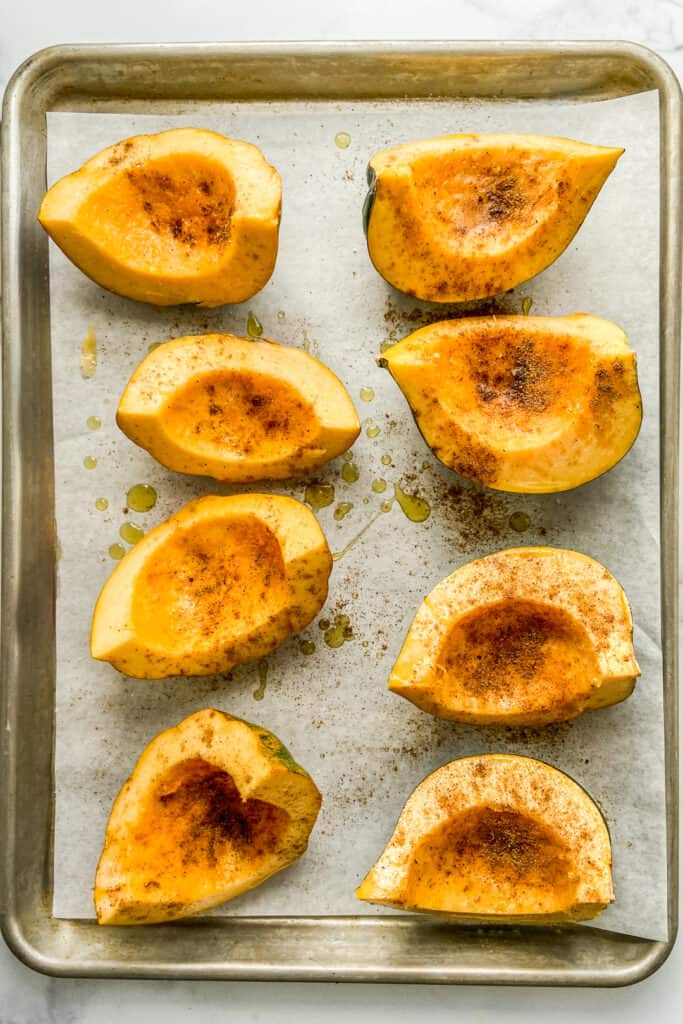 Quartered acorn squash topped with spices on a parchment lined baking sheet.