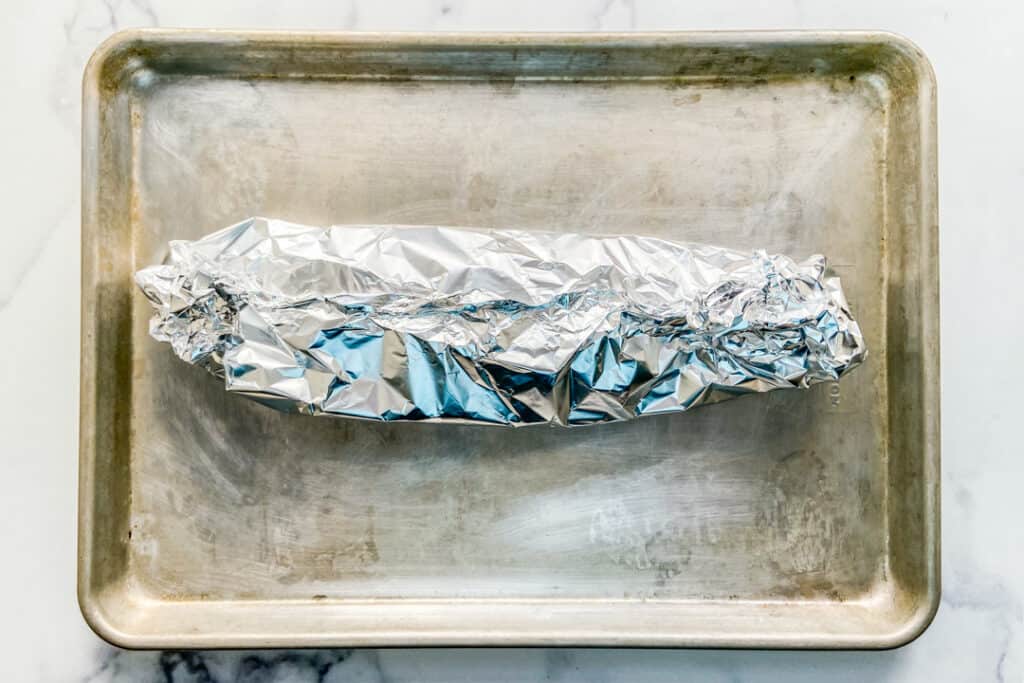 Salmon covered in foil on a baking sheet.