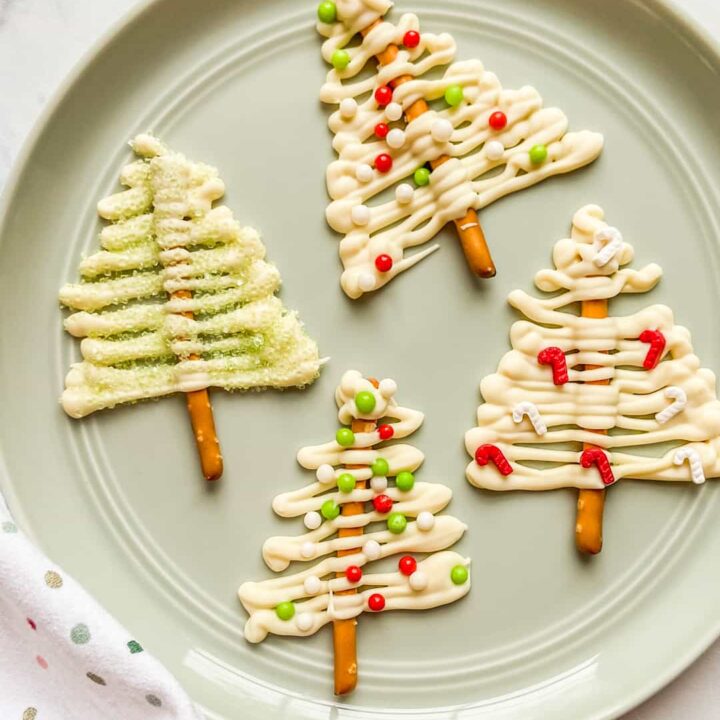 Four white chocolate Christmas trees on a light green plate.