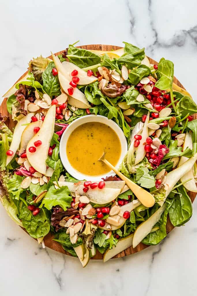 Christmas salad on a wood plate with a bowl of dijon dressing.