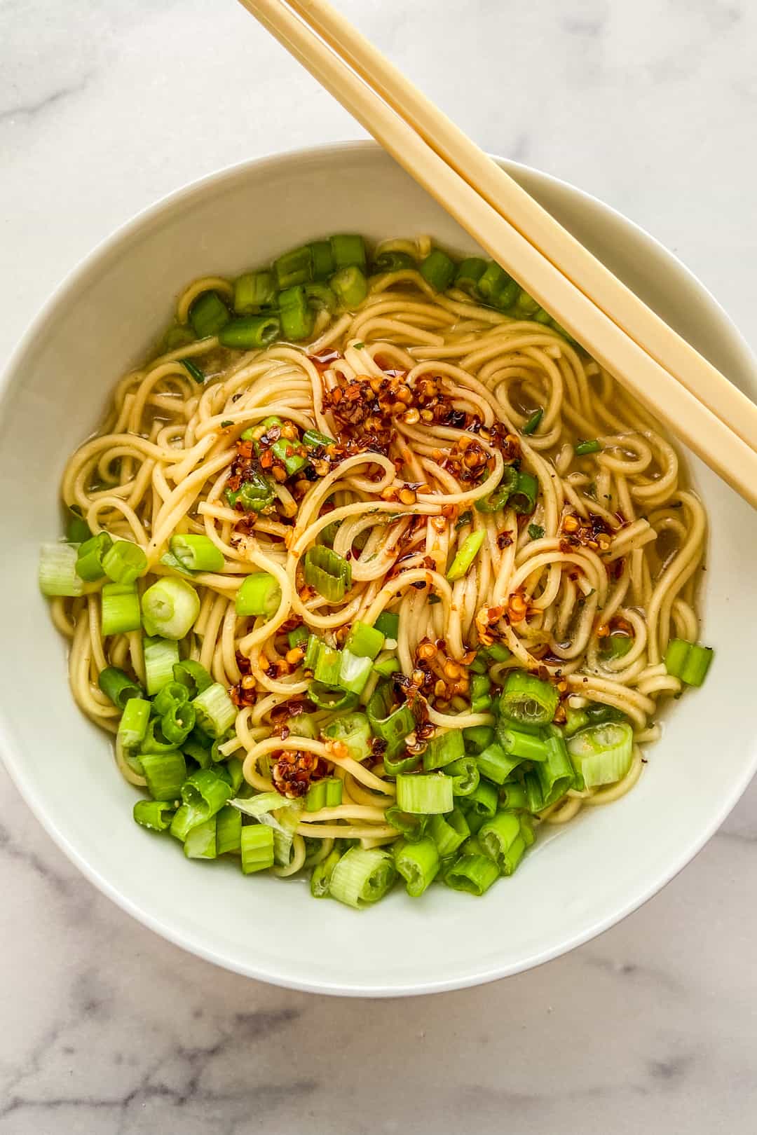 Ramen noodles in a bowl with broth, chopped scallions, and chili oil.