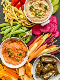 An overhead shot of a hummus board with hummus, grape leaves, cut vegetables, pita chips, and veggie straws.