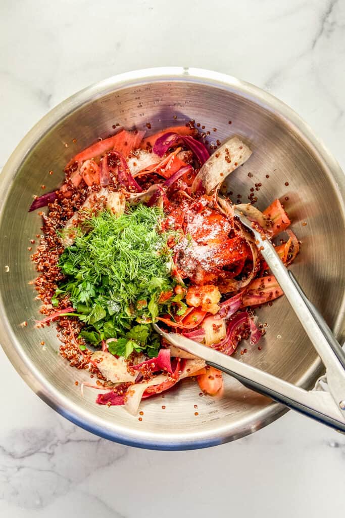 Shaved rainbow carrots, herbs, quinoa, and spices in a metal mixing bowl.