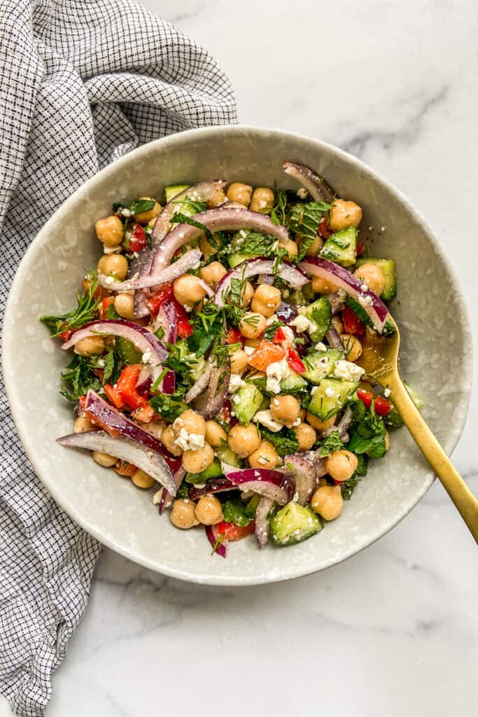 Mediterranean chickpea salad in an off-white bowl with a gold fork.