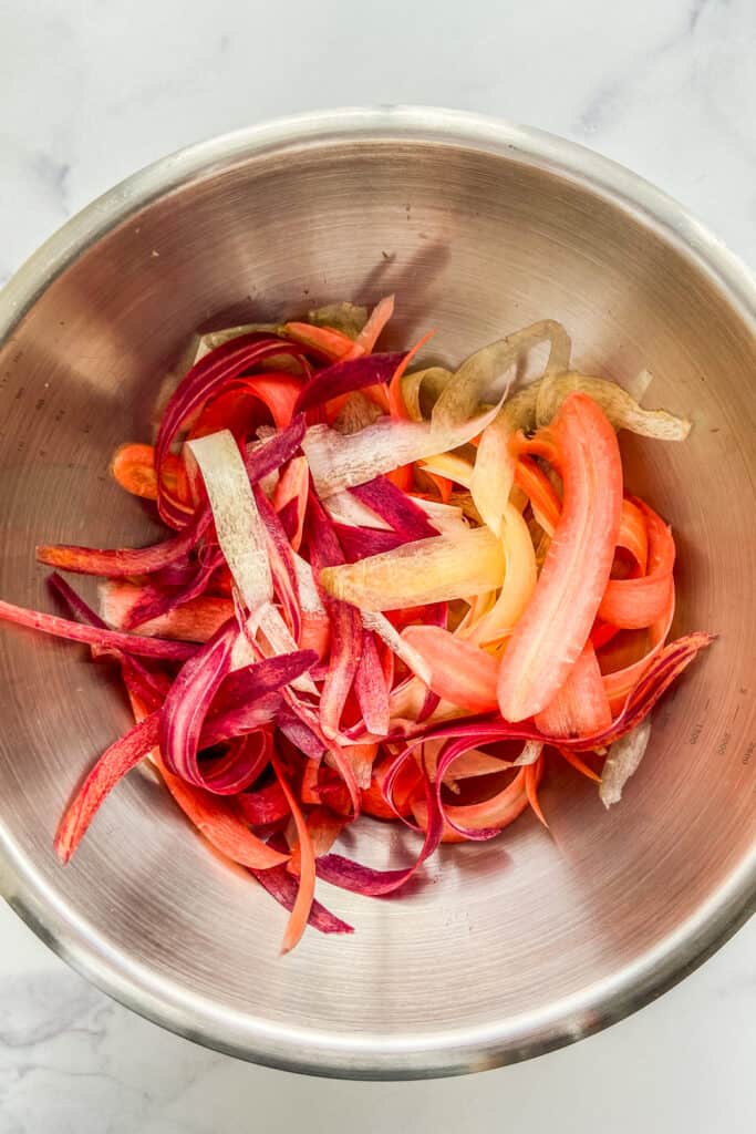 Shaved rainbow carrots in a metal mixing bowl.