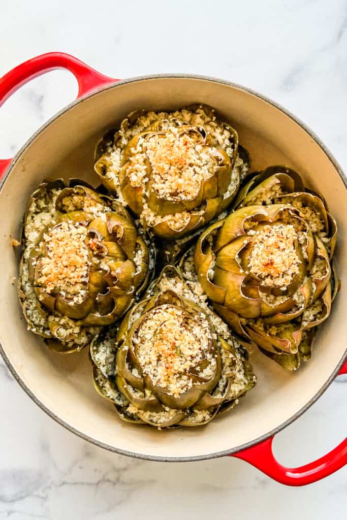 Four baked stuffed artichokes in a dutch oven.