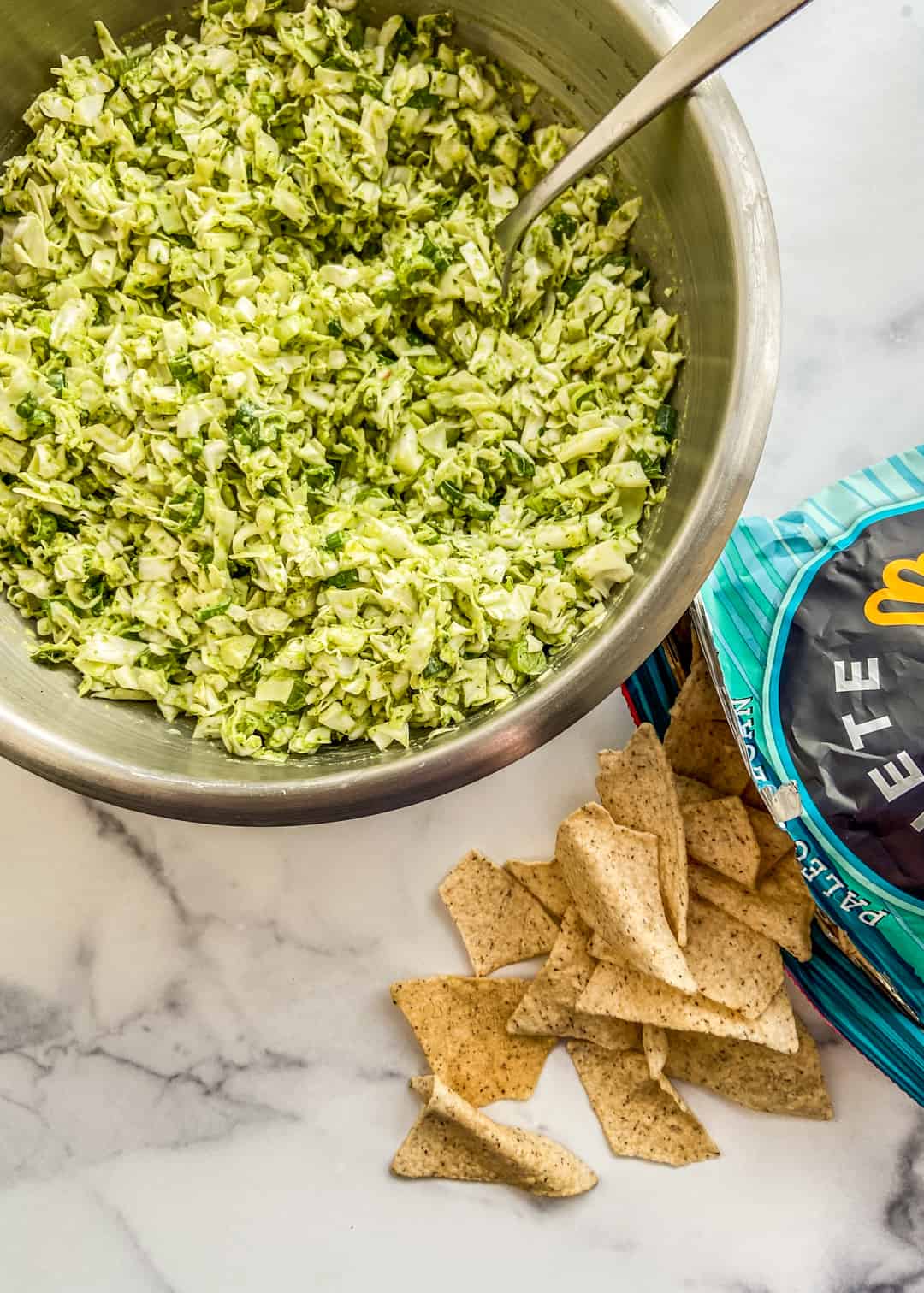 A bowl of green goddess cabbage salad next to a bag of tortilla chips.