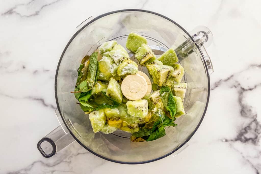 Frozen kiwi, honey, and mint in a food processor.