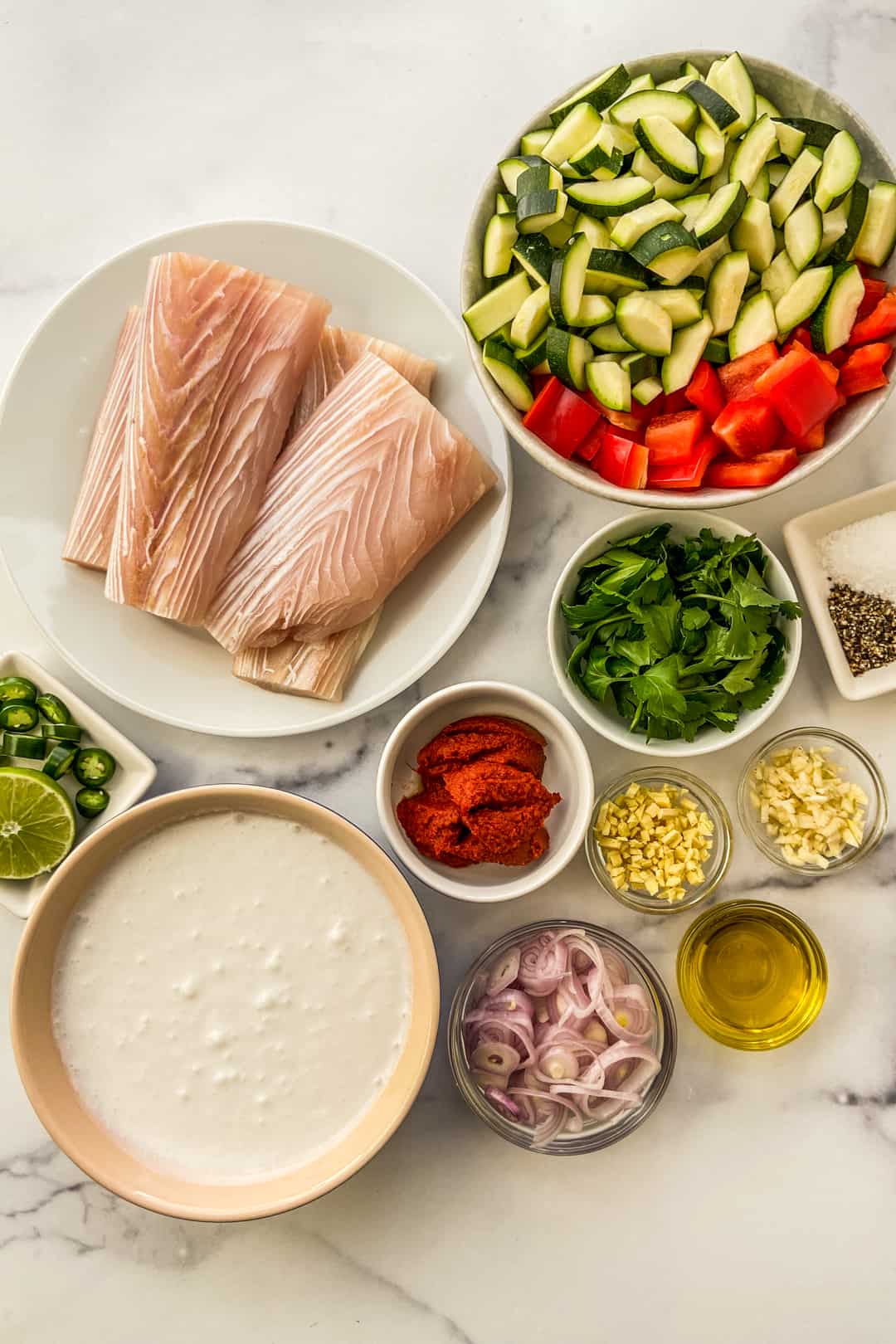Ingredients for fish curry on a marble backdrop.