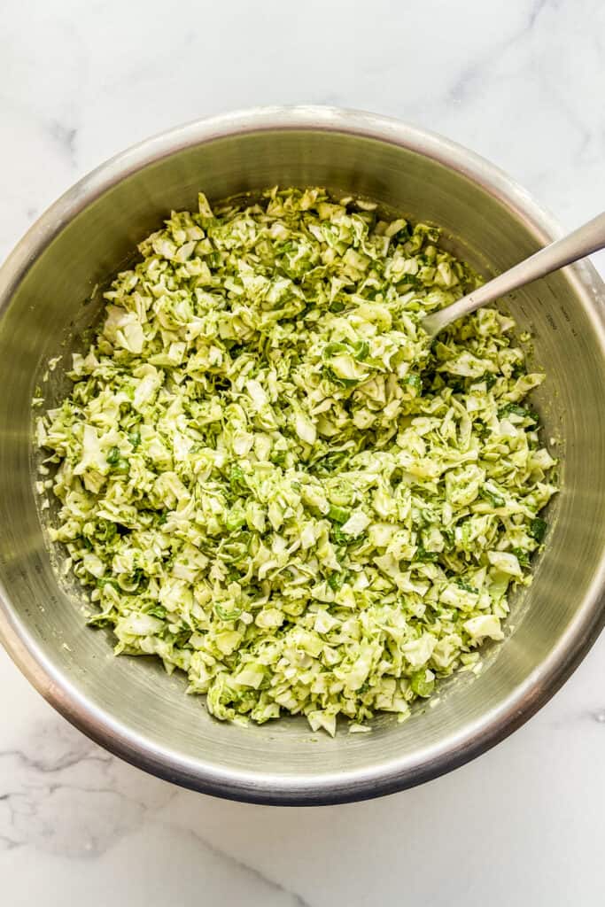 A green cabbage salad in a metal mixing bowl with a serving spoon.