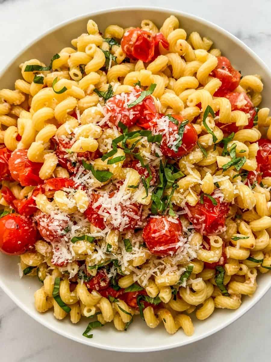Cherry tomato pasta with parmesan and basil in a white bowl.