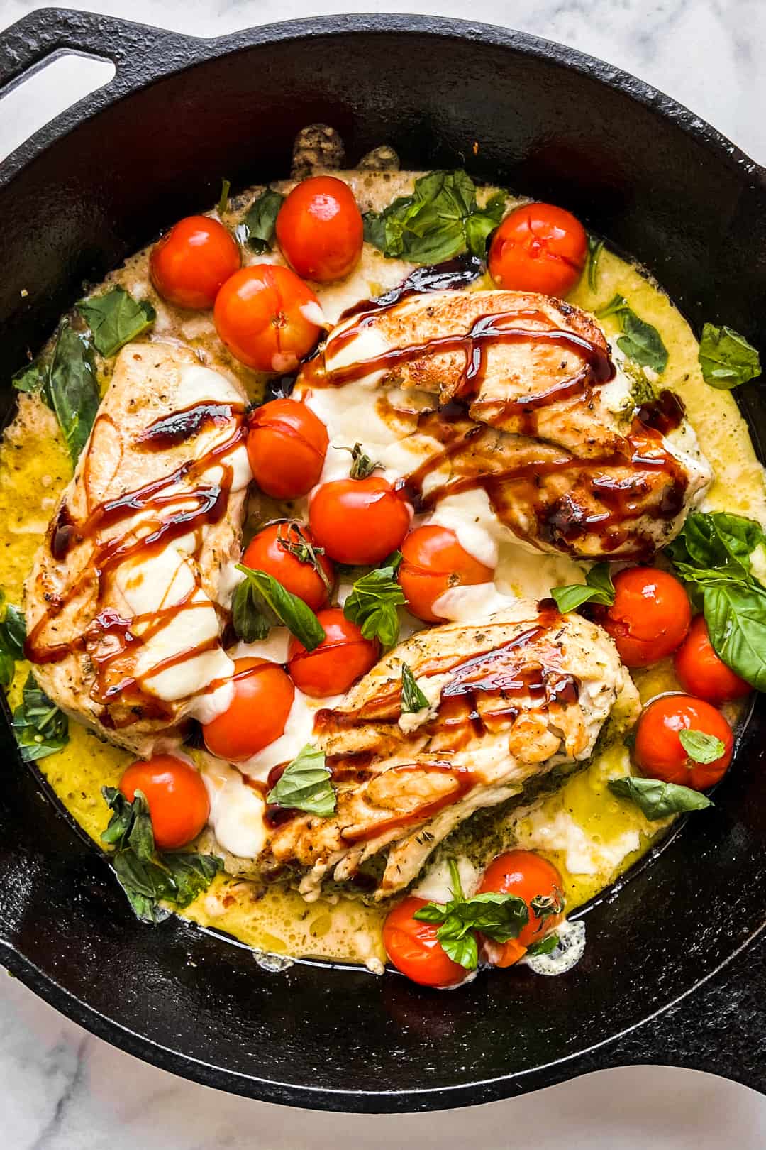 Baked Caprese chicken in a large cast iron pan.